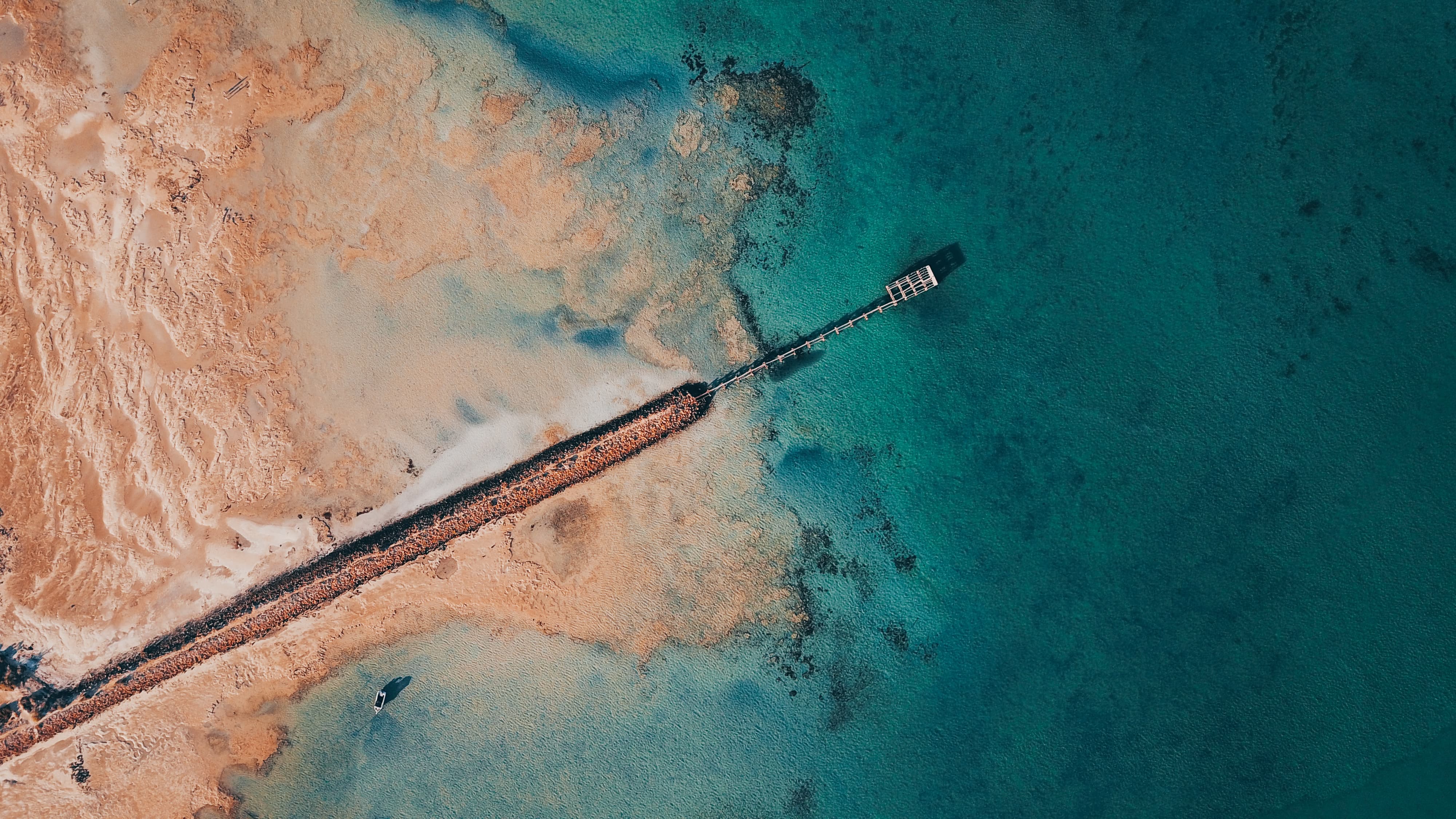 Top-down aerial drone view of a jetty over turquoise water meeting sand