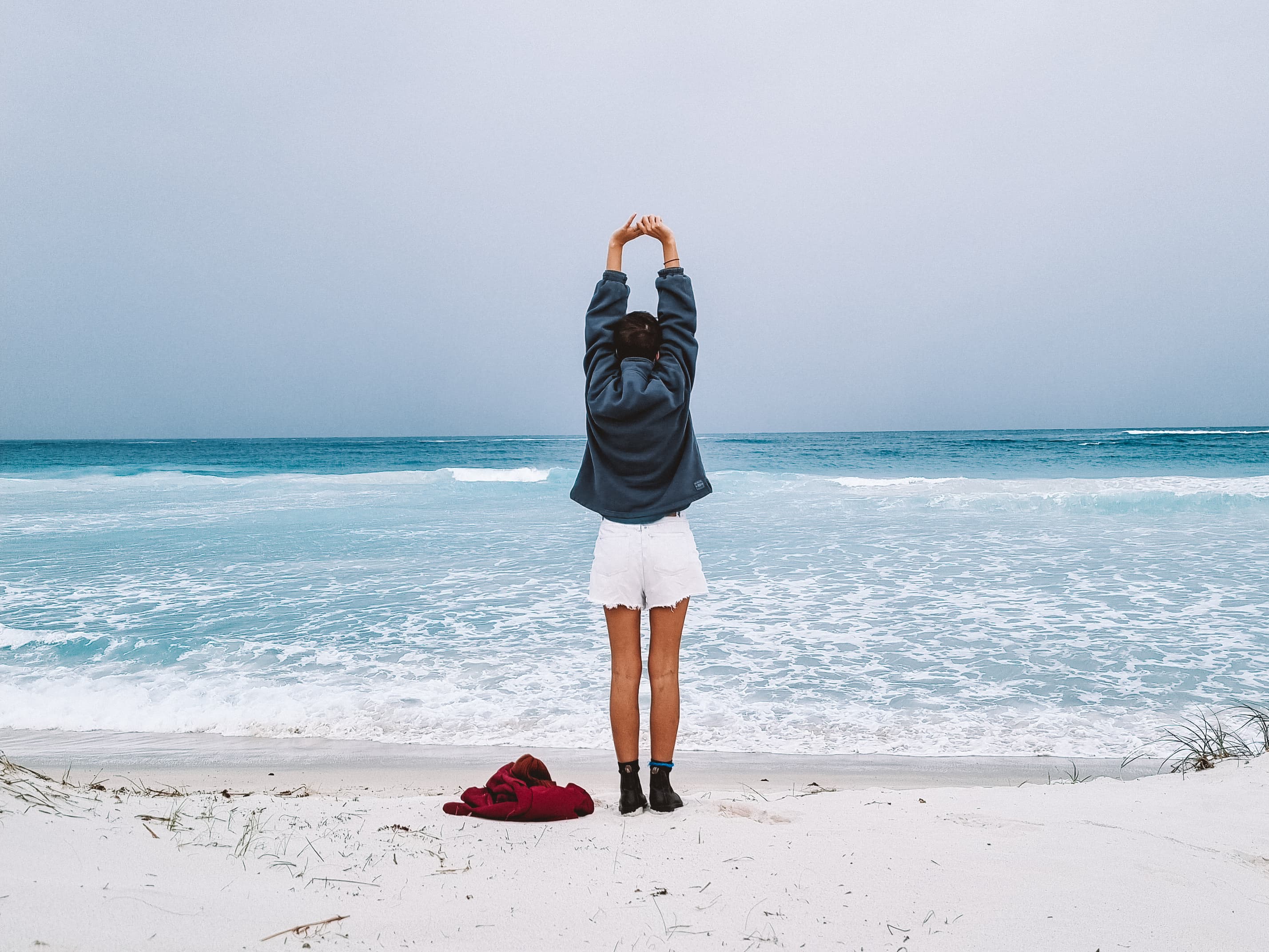 A person stretching at the beach, facing the horizon